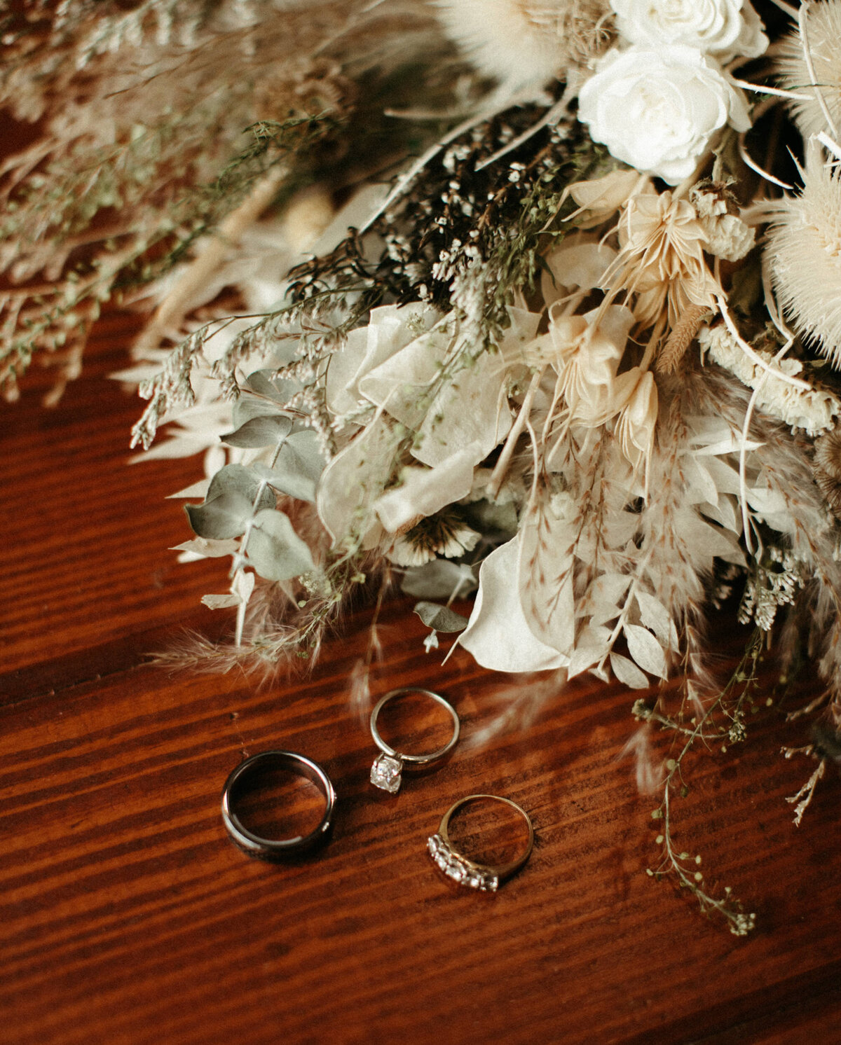 Wedding details of bands and engagement ring laying next to dried floral bouquet