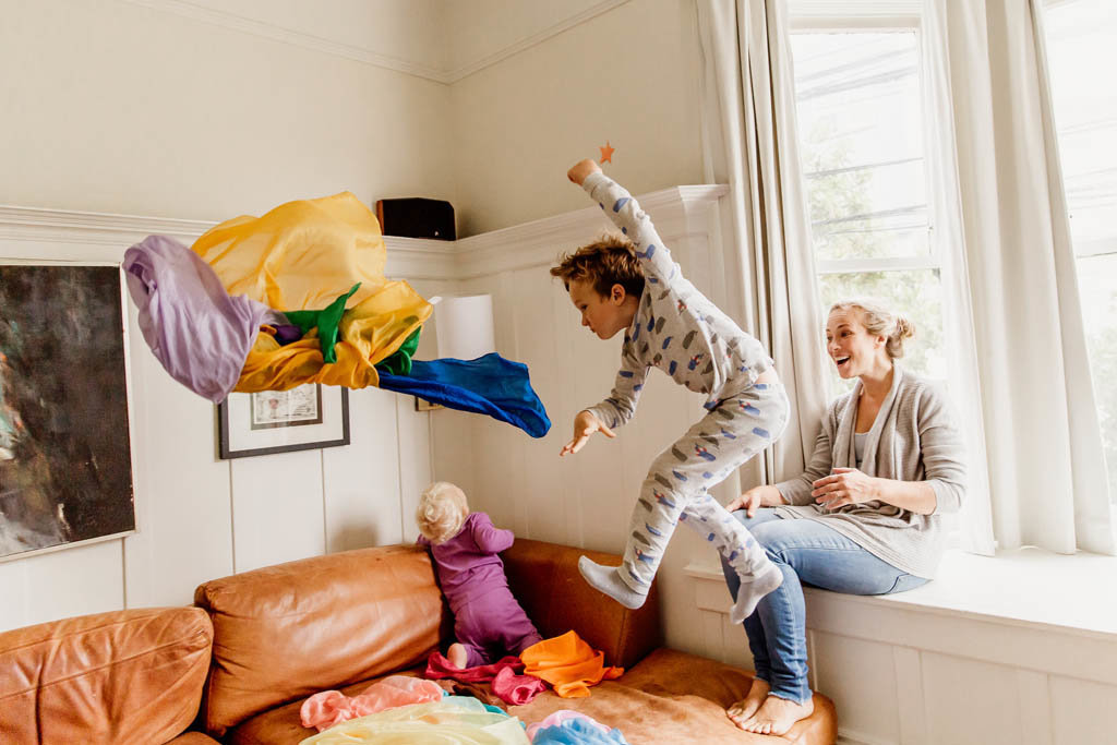 San francisco child jumps and throws rainbow silks while jumping off couch during playful in home family photography session