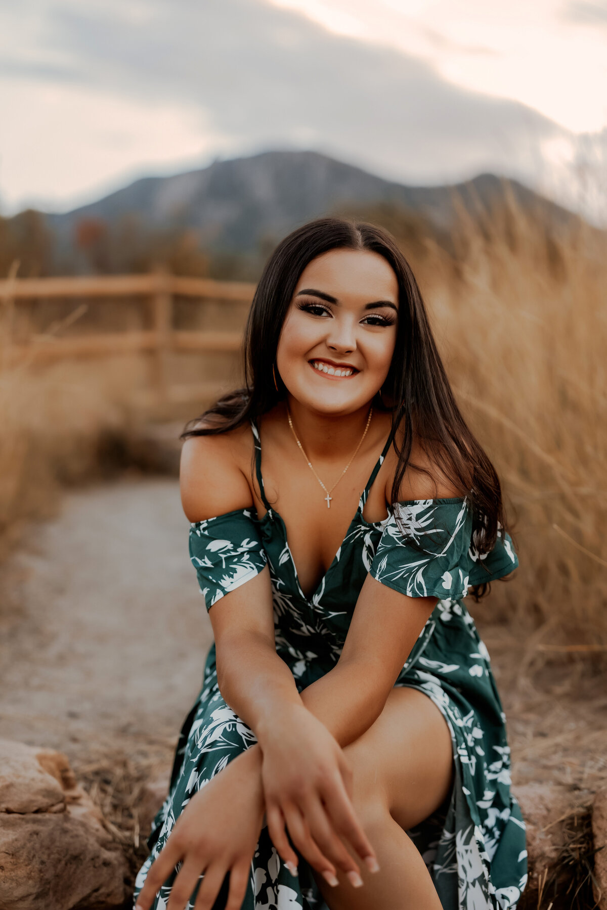 senior girl sits on ricks with mountains behind her in a green dress for her senior photos