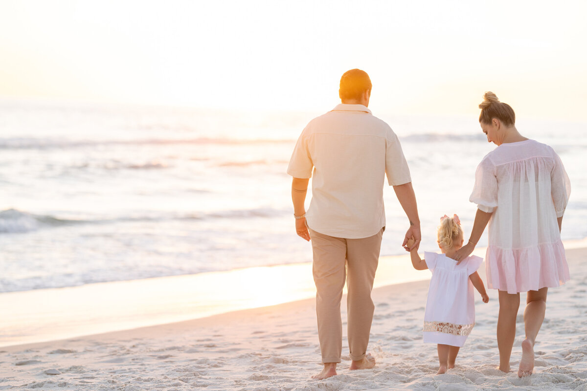 Two parents holding their child's hands while walking at the beach