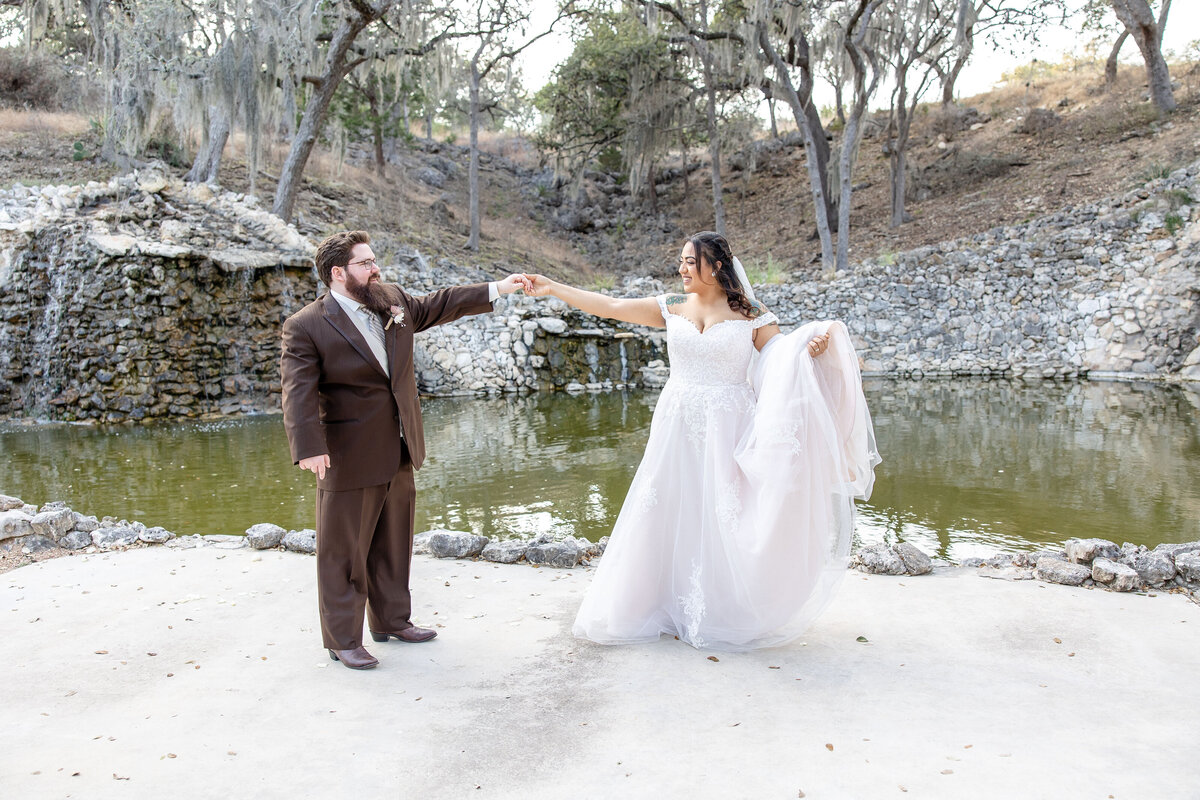 bride and groom dance in front of waterfall at hill country wedding