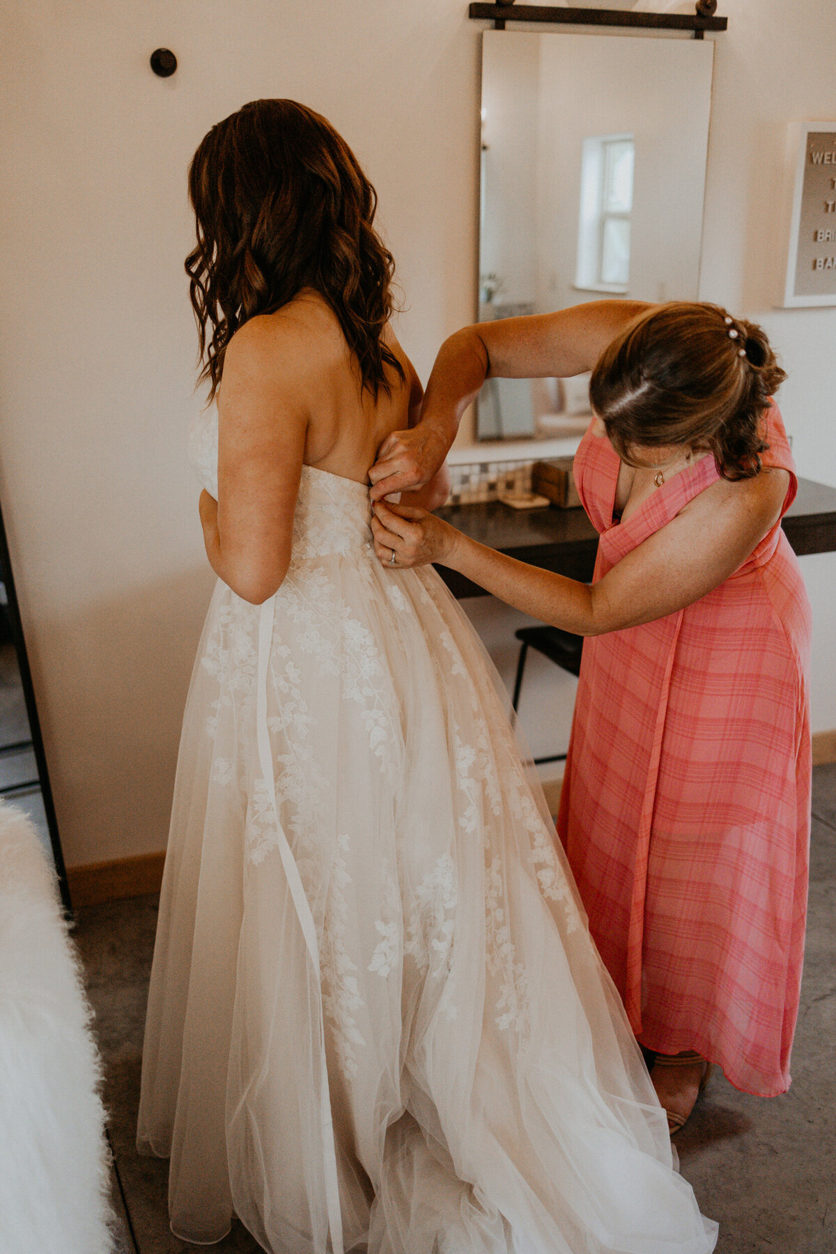 bride and her mom getting  in her wedding dress