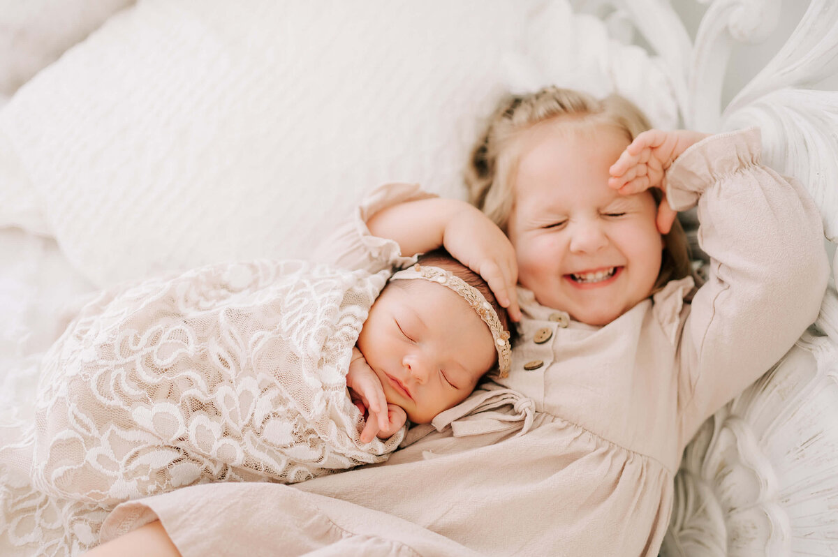 sister cuddling and smiling in bed in Springfield MO newborn photography studio