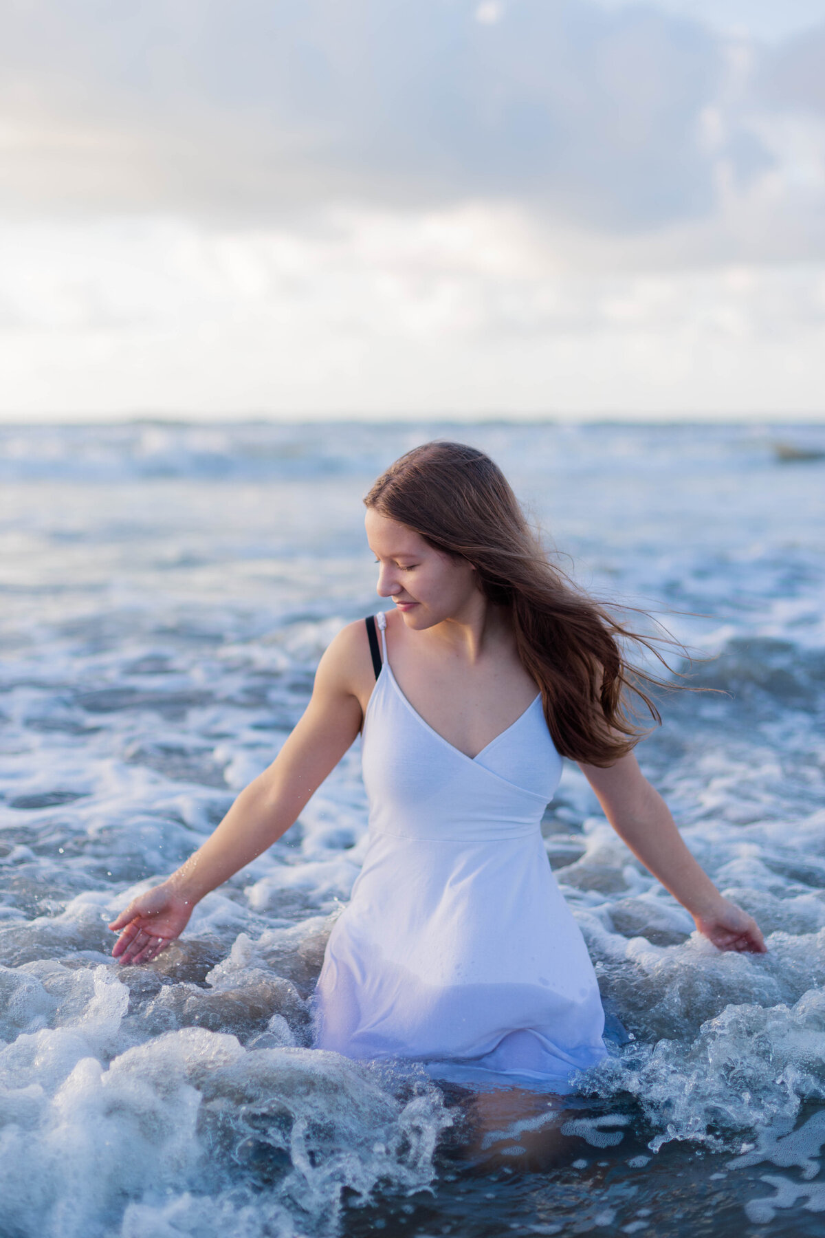 Girl kneels in the waves on Galveston Beach wearing a white dress