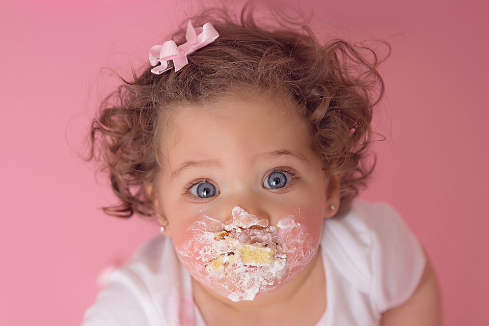 A toddler girl with a mouth full of cake and face covered in icing