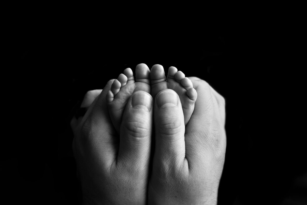 Katie Marhsall, New Jersey's premier newborn baby photographer captures a detail image from a newborn photoshoot. Balck and white. Dad is holding baby's feet to show scale.