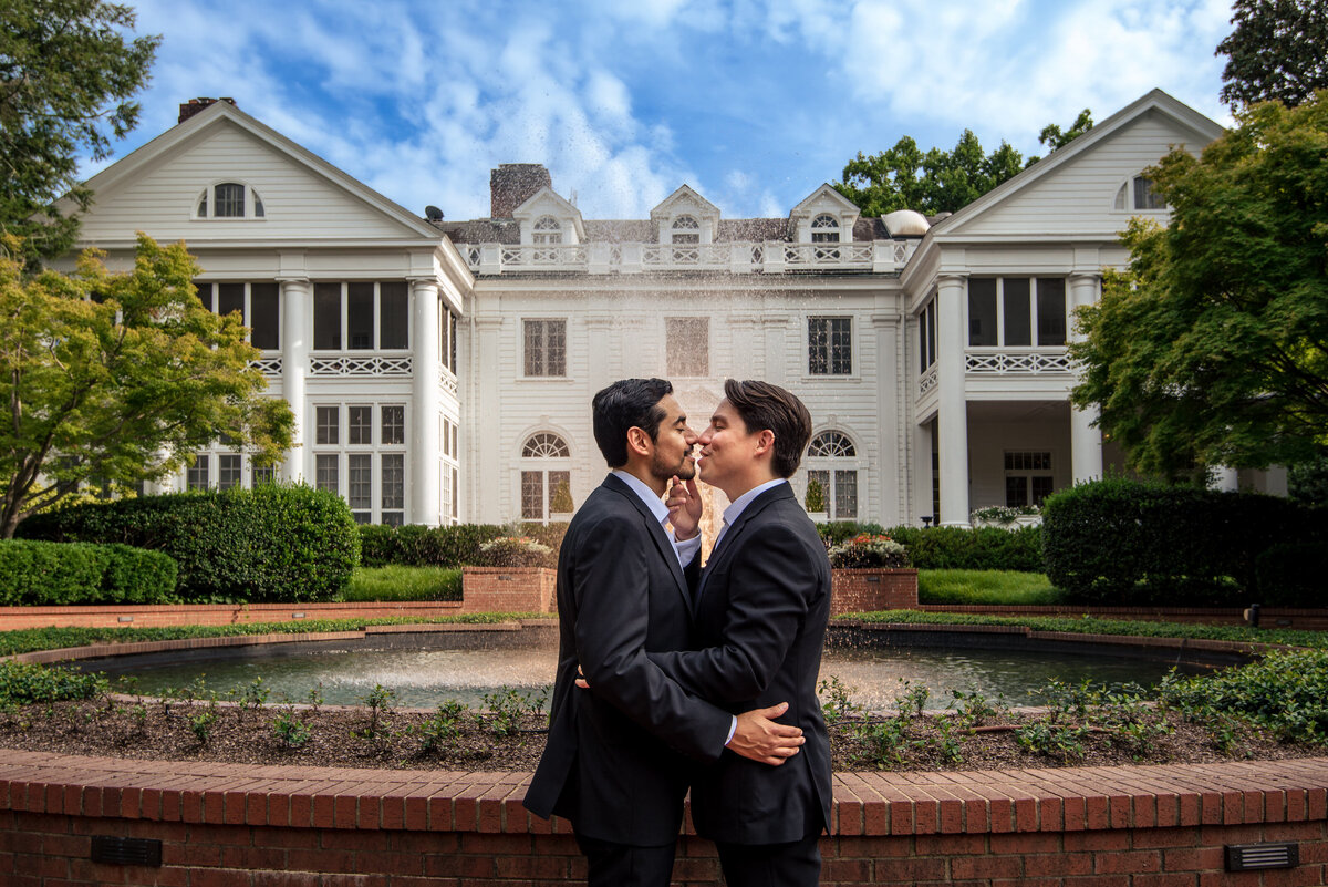 LGBTQ+-couple-with-arms-around-each-other-smiling-just-before-a-kiss-standing-in-front-of-the-Duke-Mansion