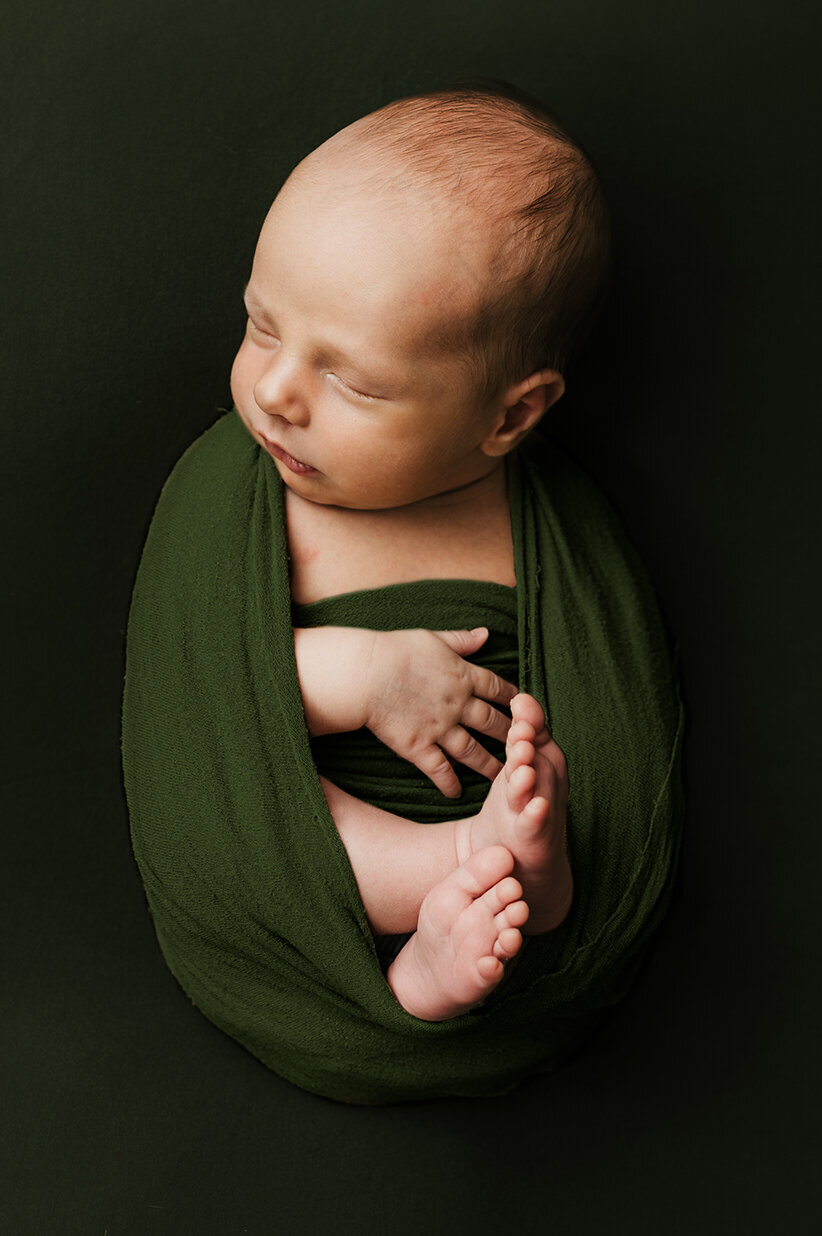 Sleeping baby laying on a green background wrapped in green