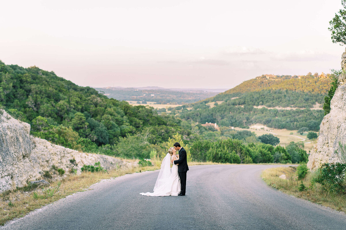 Newly married husband and wife kiss while overlooking Texas hill country landscape