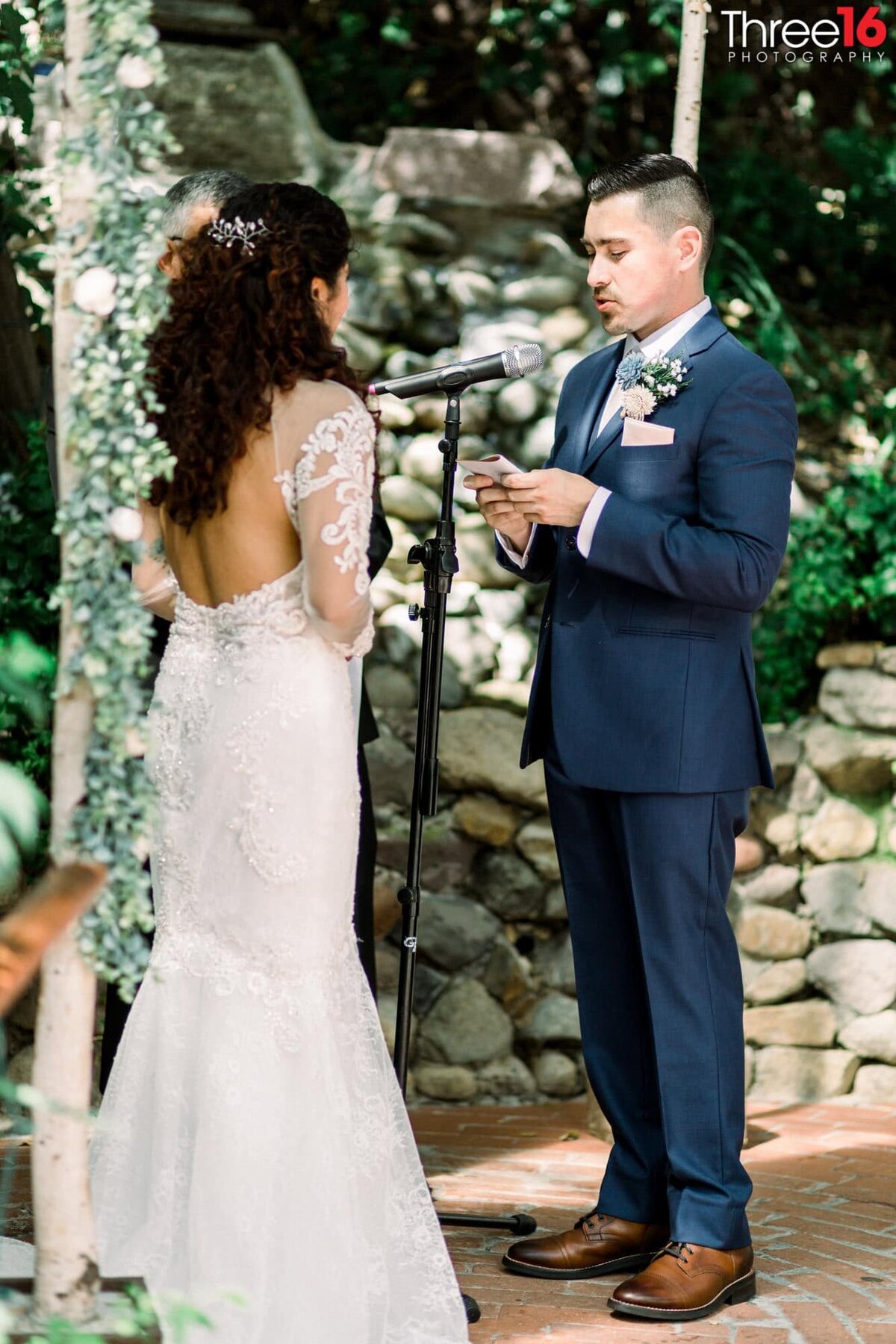 Groom stands at the altar reading his vows into a microphone to his Bride