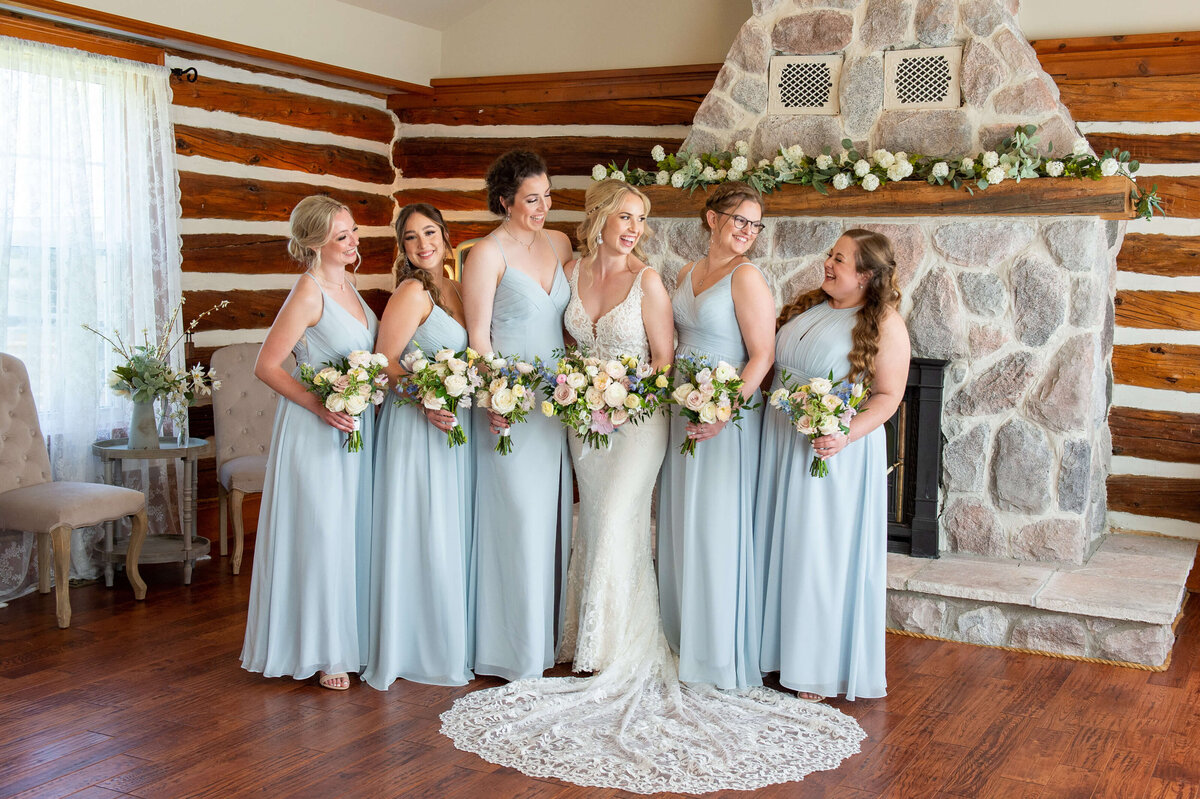 full length photo of bride and her bridesmaids dressed in blue holding bouquets in the Stonefields Estate Farmhouse. Captured by Ottawa wedding photographer JEMMAN Photography