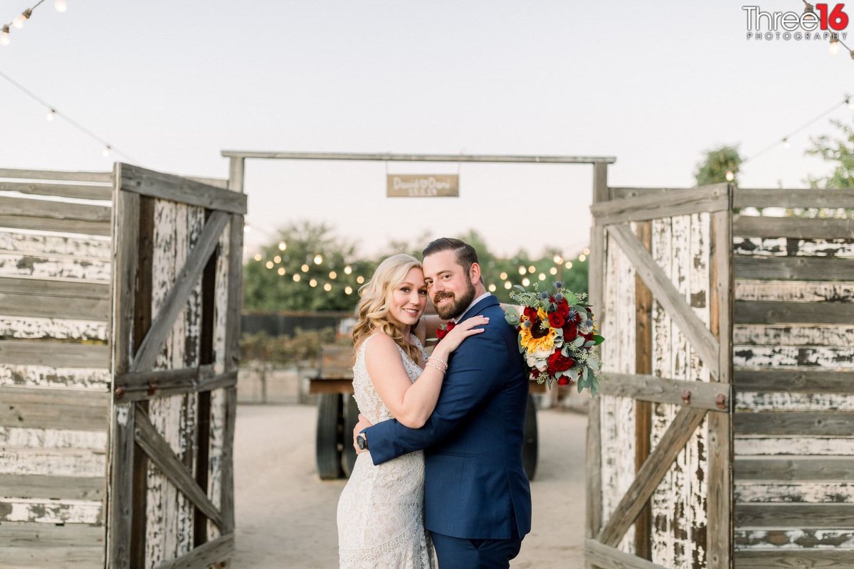 Bride and Groom pose together in front of the open ranch-style gates that lead into the reception area