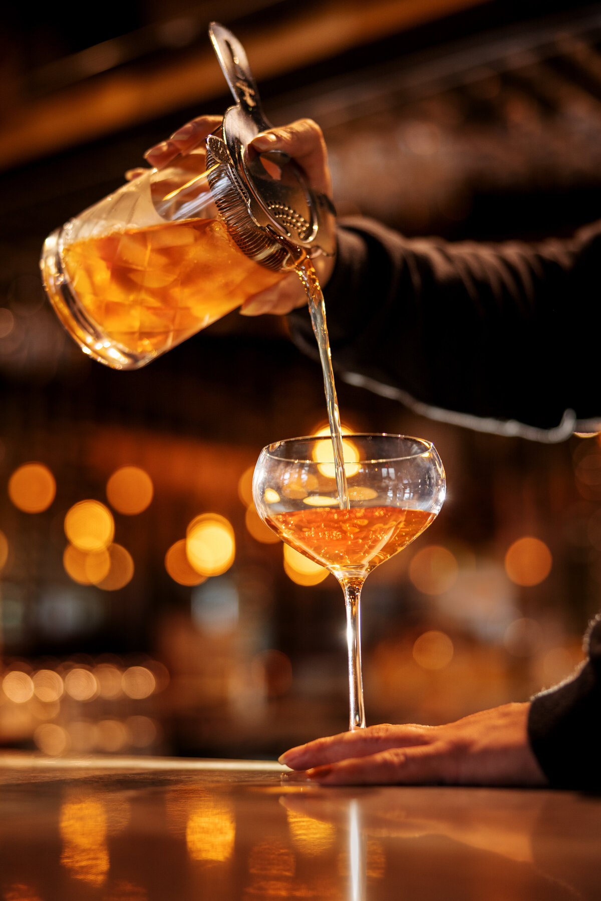 A cocktail being poured into a stemmed glass