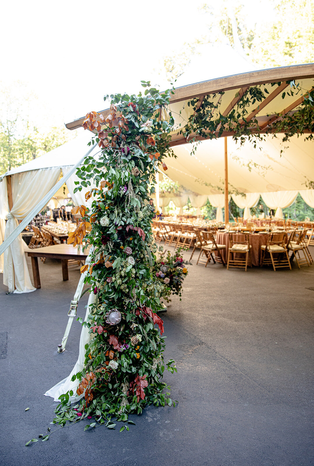 Tent entrance flower installation with lush vines, hops, fruiting pomegranate branches, greenery, wildflowers in shades of pink, mauve, copper, golden yellow, and soft blue. RT Lodge luxury wedding floral designer.