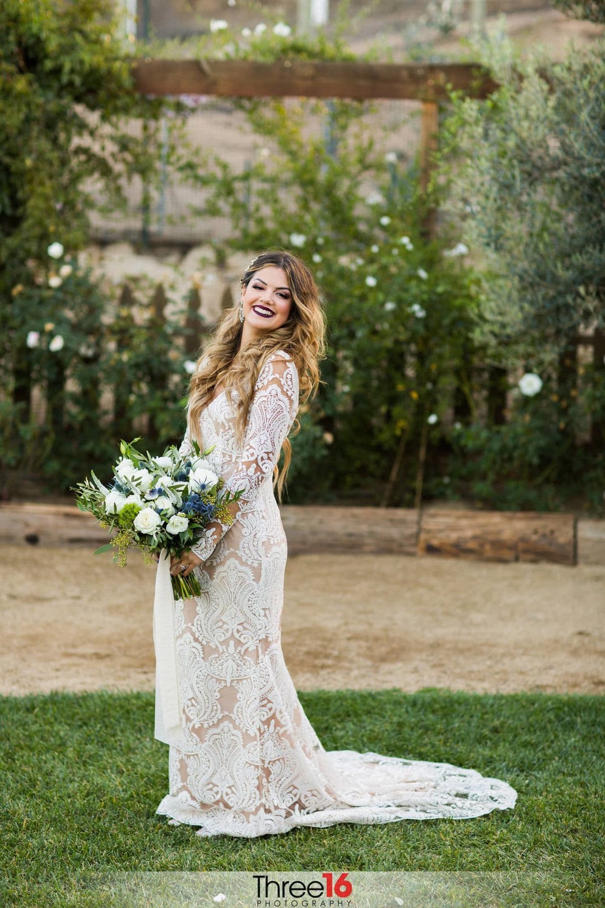 Bride poses on the grass with her bouquet and dress train fanned out