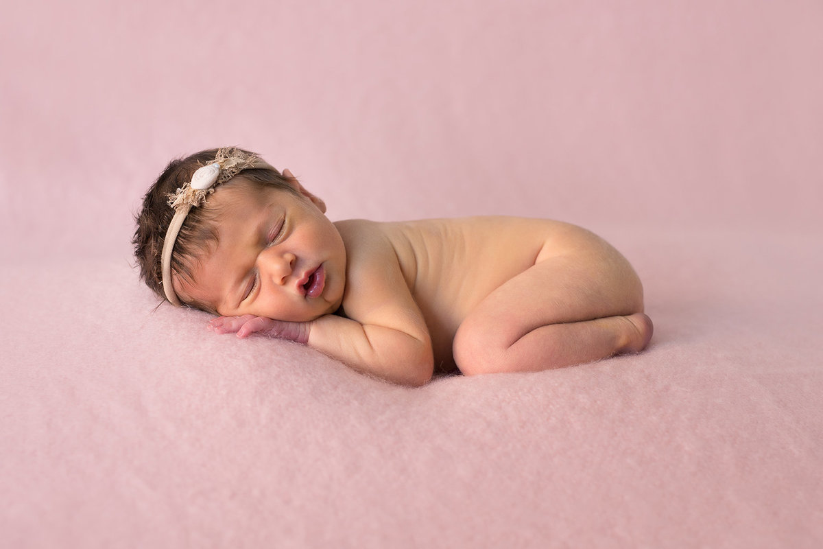 a newborn girl sleeping on a pink blanket