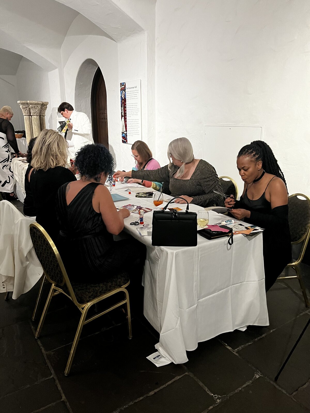 People sitting at a table, cutting, gluing, and arranging images for their collages