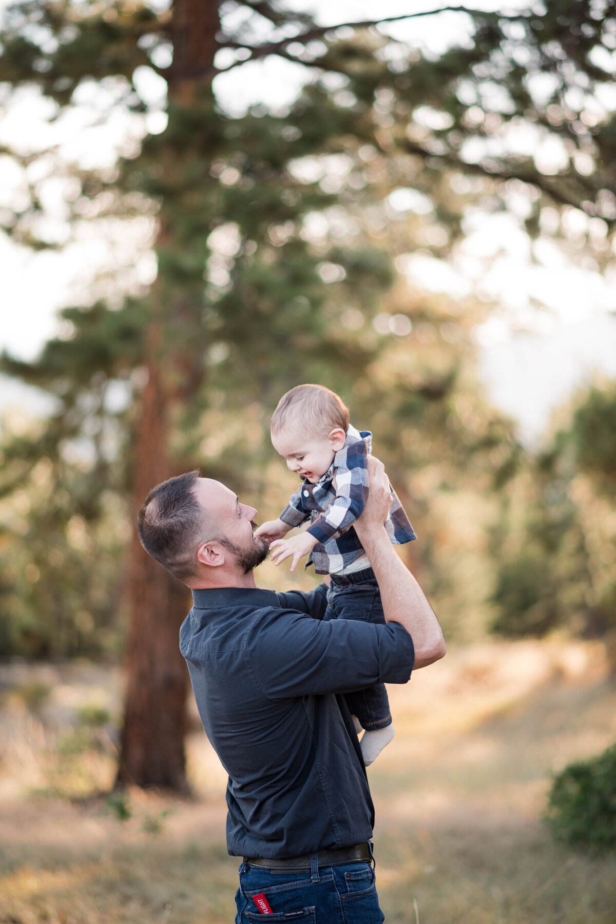 father holding his toddler son up in the air for their family photos denver in the woods for fall family photos