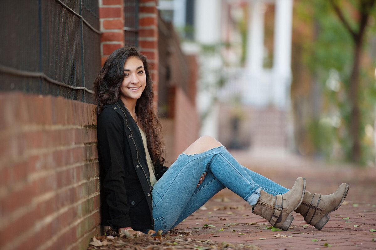 Senior session of young woman sitting near a brick wall