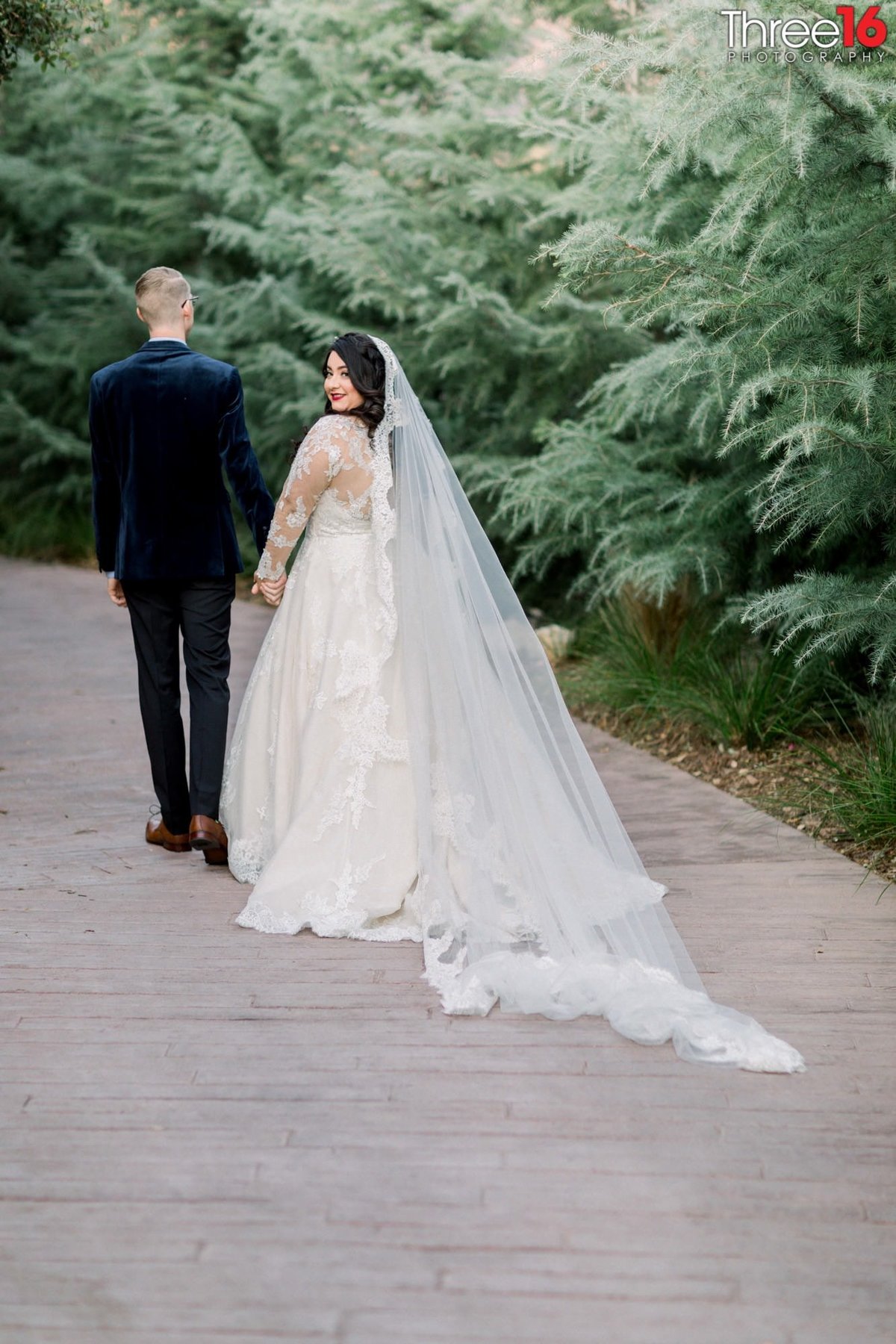 Bride looks back as she walks hand in hand away down a path with her Groom