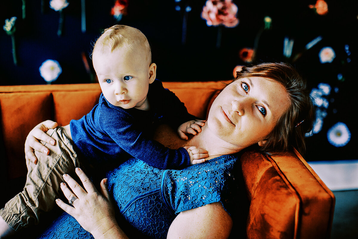 a mom holds her young son while she sits on a velvet couch