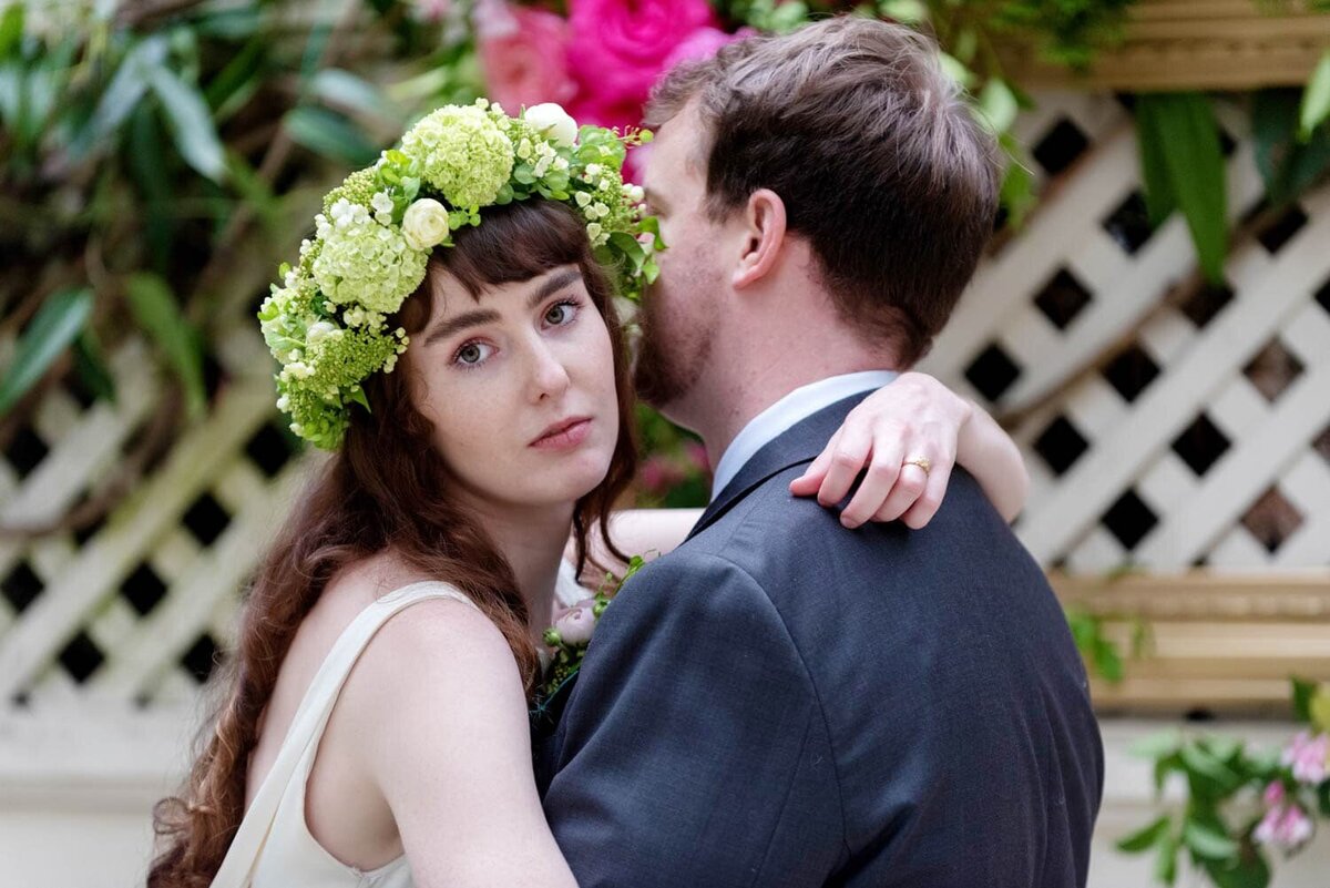 a pretty bride hugs a man while looking at the camera wearing a green flower crown