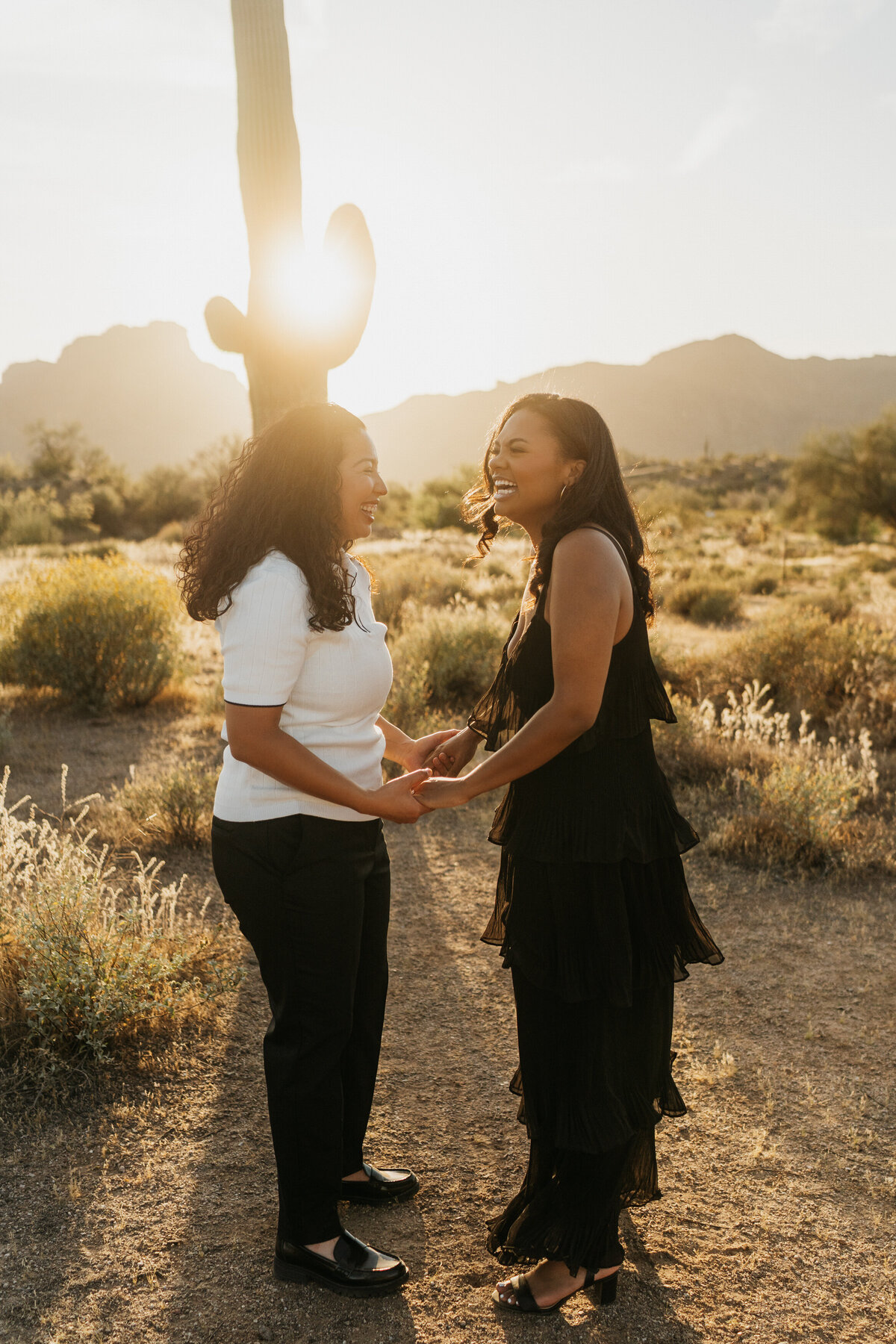 A couple holding hands and laughing in the desert at sunset 