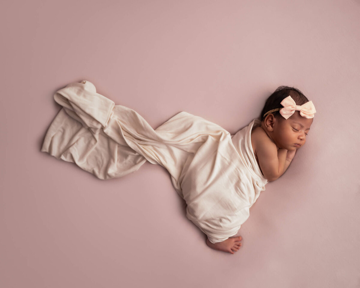 A newborn baby girl sleeps with fabric flowing behind her