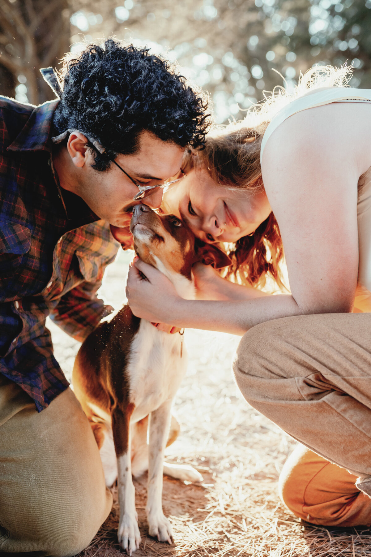 Enchanting engagement photoshoot during golden hour at Lighthouse Park, Santa Cruz, featuring a joyful couple sharing a tender moment with their beloved dog