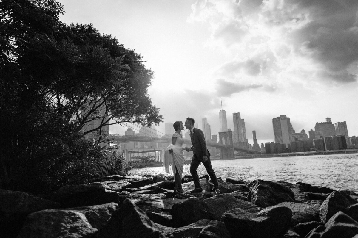 A wedding couple kissing while standing on rocks along the water.