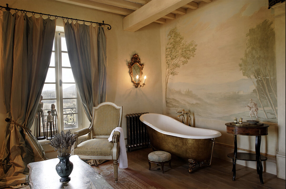 A bronze-brushed slipper bath beside a hand-painted scenic mural at Borgo Santo Pietro