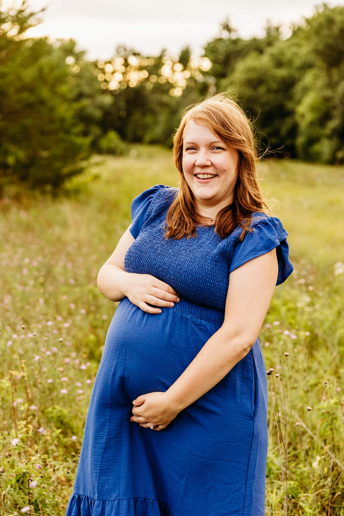 beautiful first time mom holding bump in a wildflower field and laughing by Green Bay Maternity Photographer Ashley Kalbus