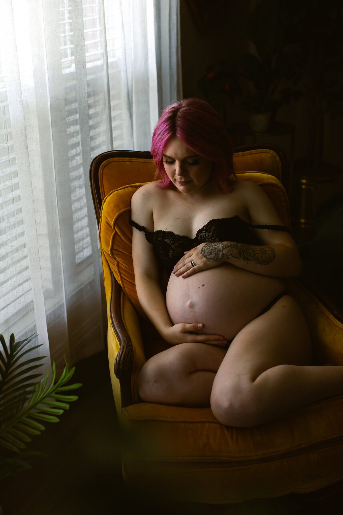 In a sunlit studio, a glowing pregnant woman poses for a maternity boudoir session, showcasing her baby bump