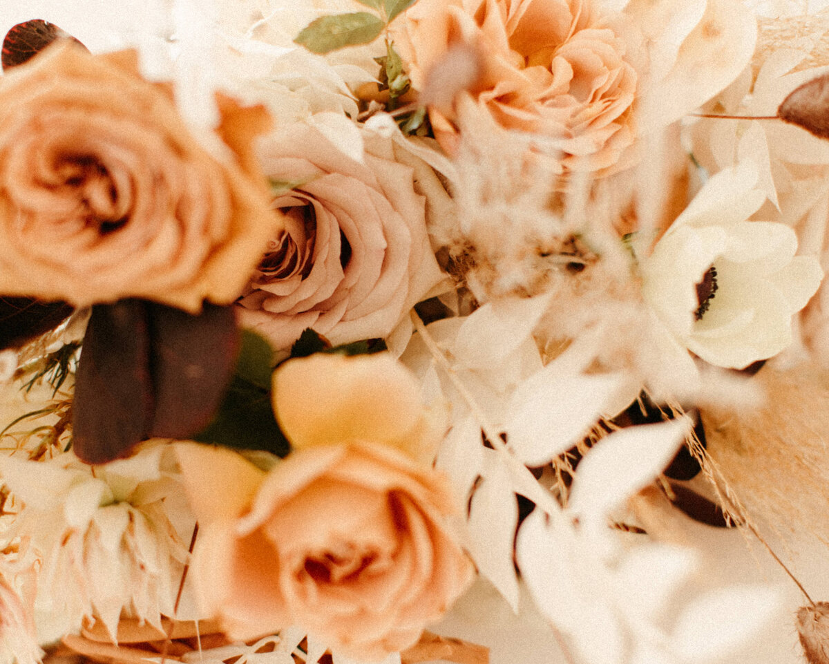 Coral and peach colored roses with neutral dried floral accents in bridal bouquet