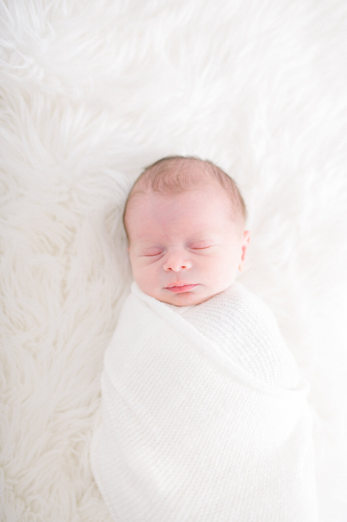newborn boy sleeps while being wrapped for his portrait. Captured in studio by Niagara newborn photographer Kristine Marie Photography