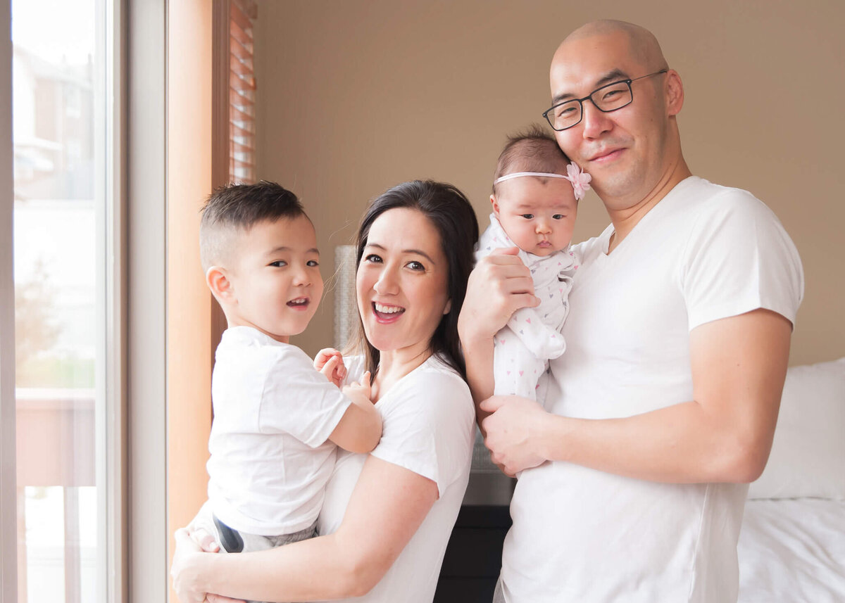 adorable family with little son and new baby in pajamas in master bedroom by sliding glass door