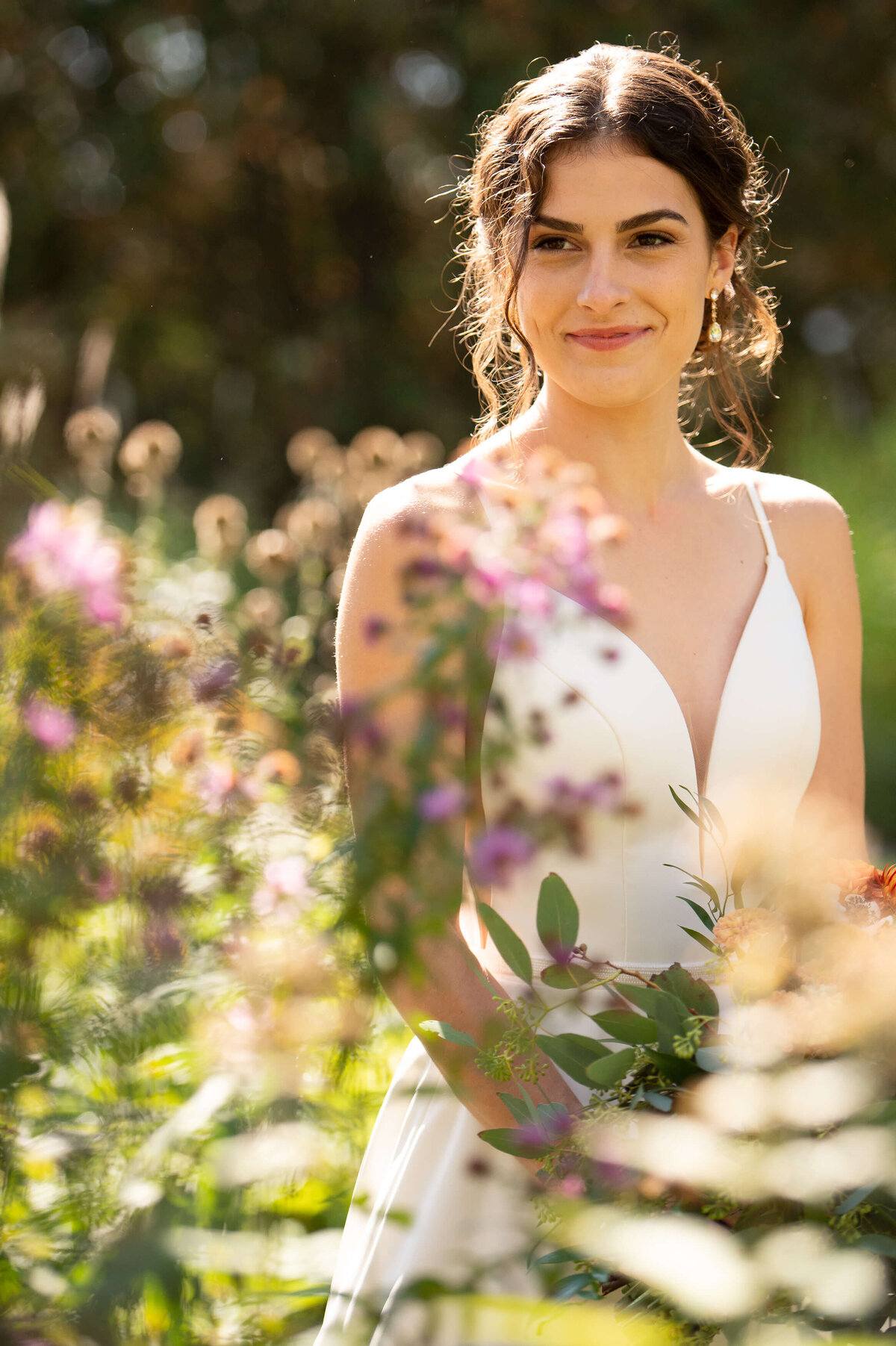 a sunny backlit portrait of a bride smiling in the gardens of Strathmere wedding venue in Ottawa.  Captured by Ottawa wedding photographer JEMMAN Photography
