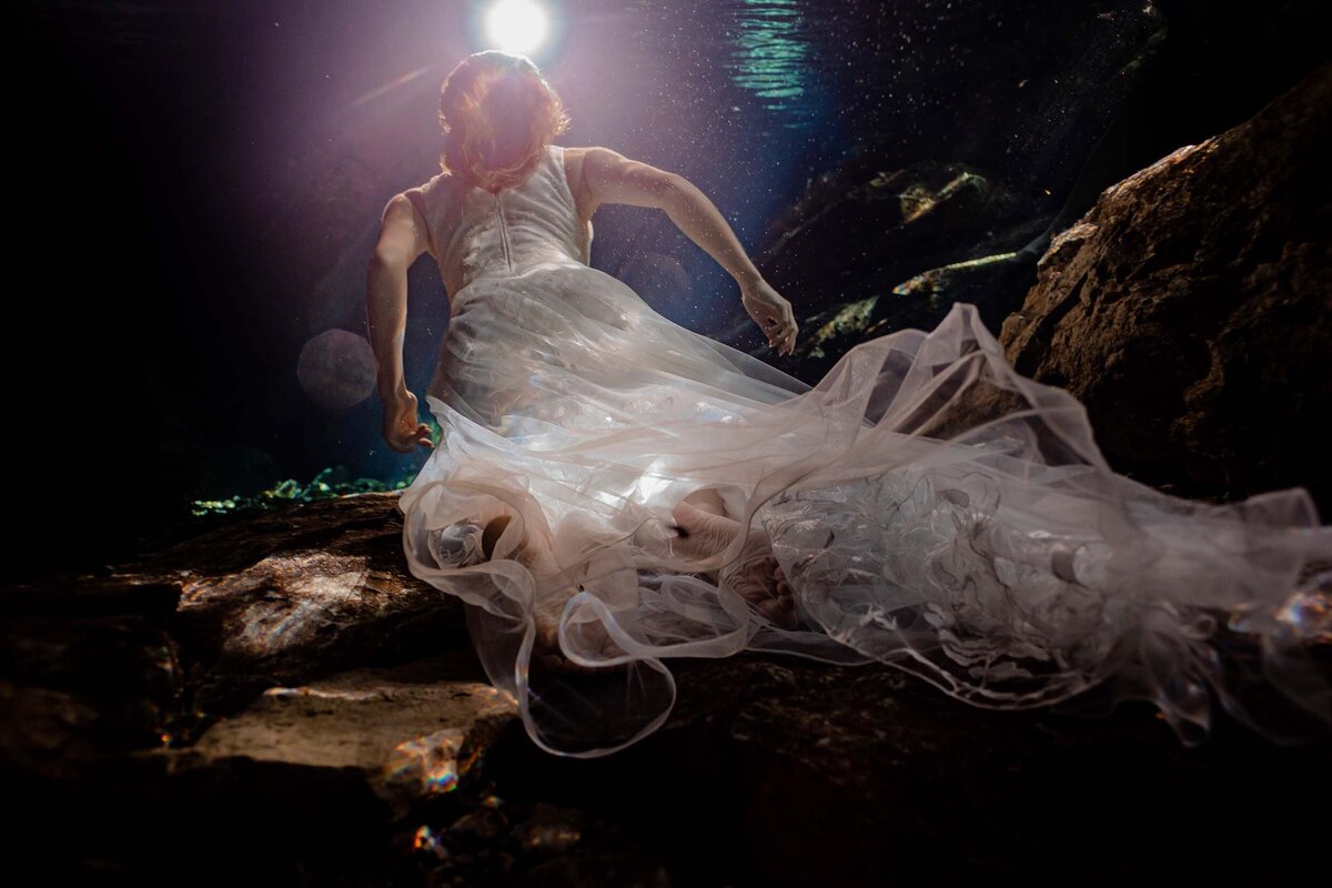 Bride swimming towards light with dress flowing .