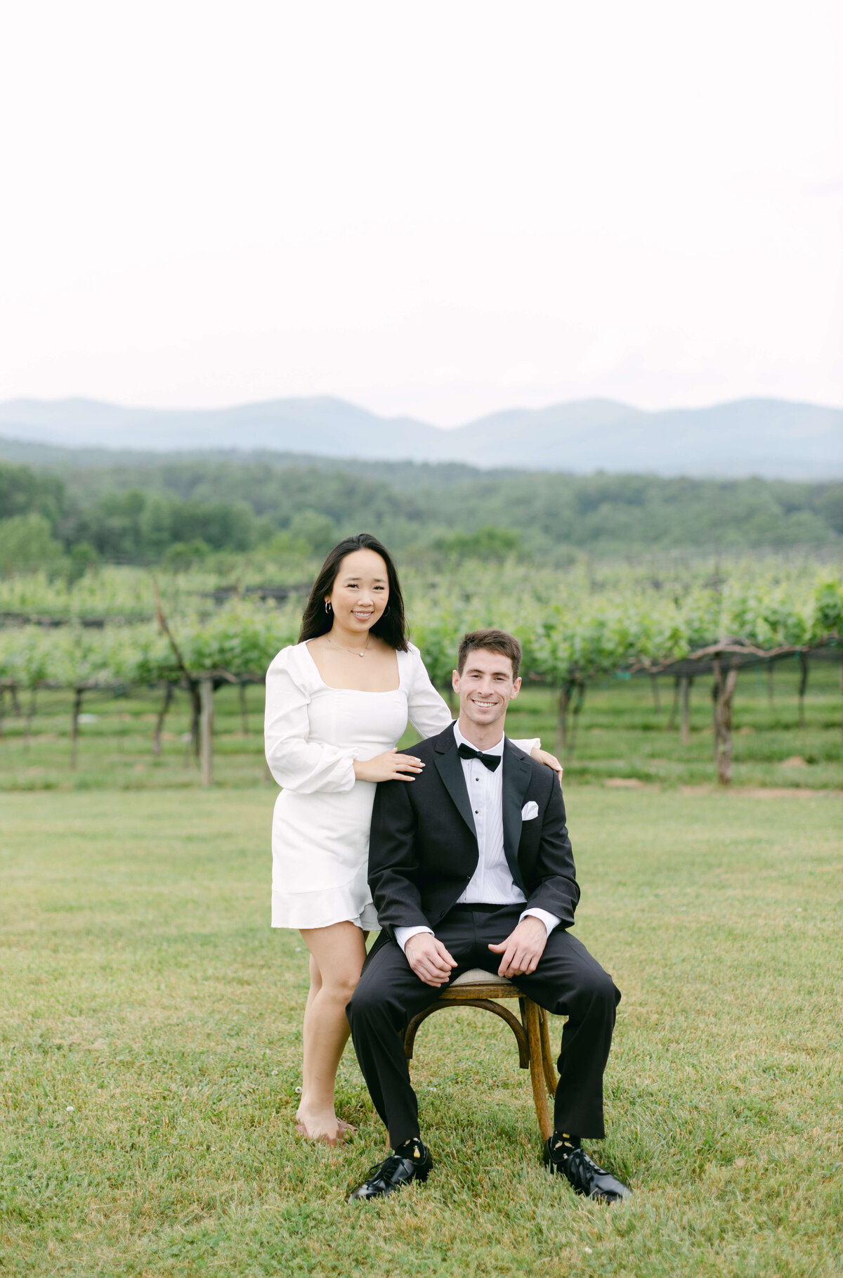 A groom sits in a chair while his bride stands over him.