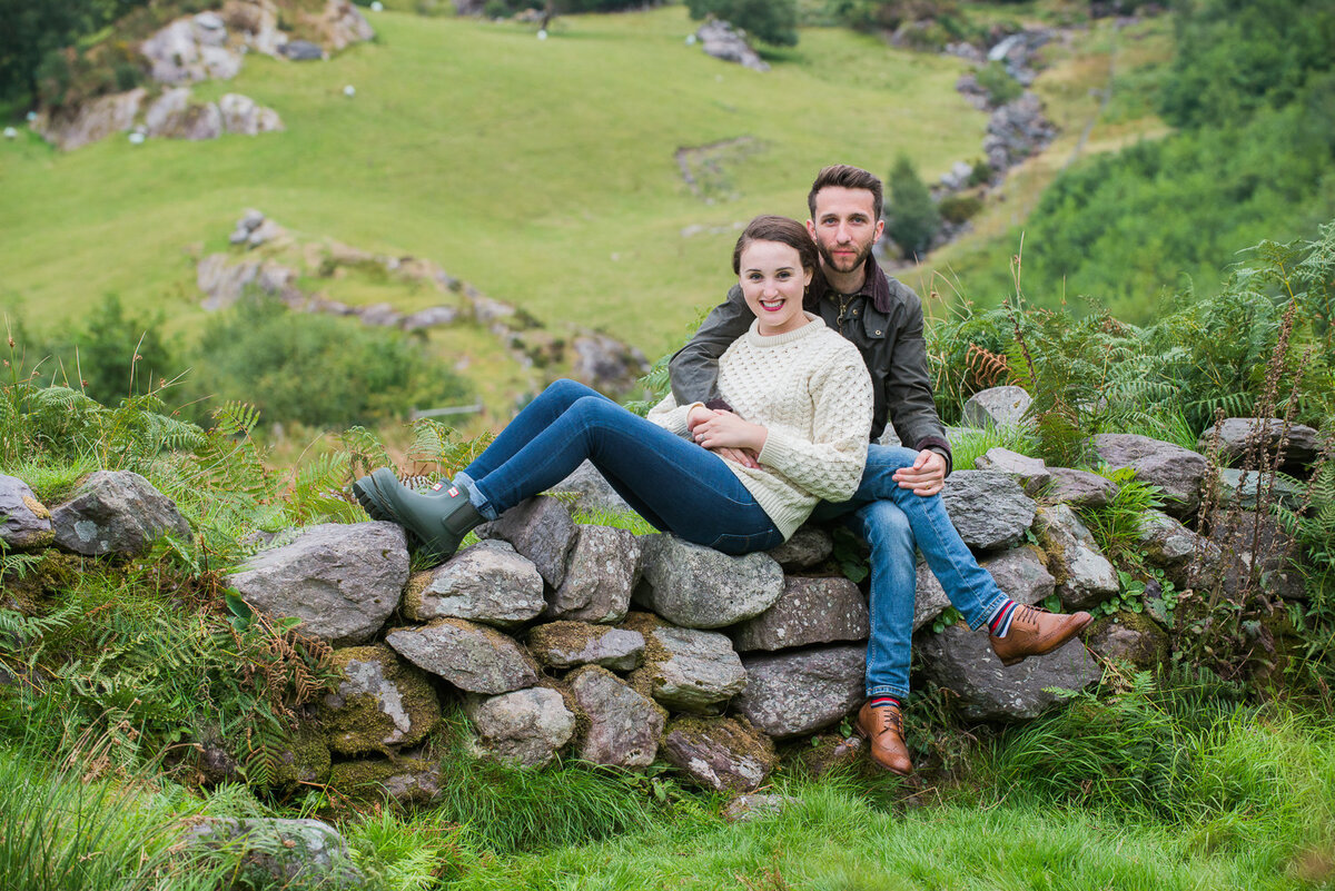 Young couple in aran sweater and jeans relaxing on an old stone wall in Kerry
