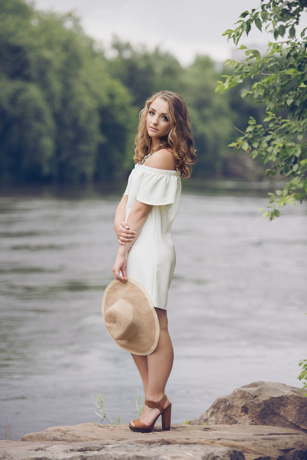 Chanhassen senior photo of girl by river with a white dress and hat