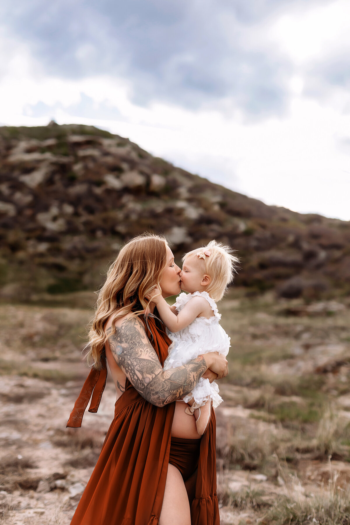 mom holding her toddler girl over her bump as they kiss for photos