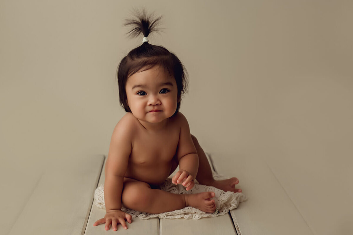 one year old sitting nude on cream hardwood floor