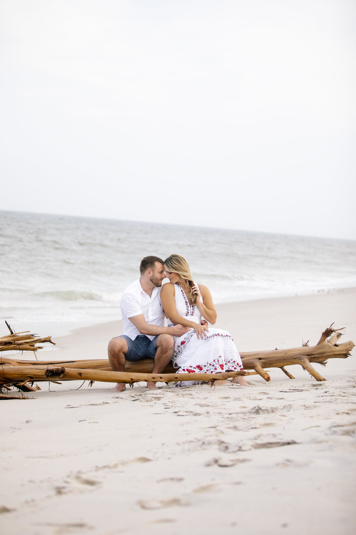 engaged couple sit on beach on driftwood  at LBi session