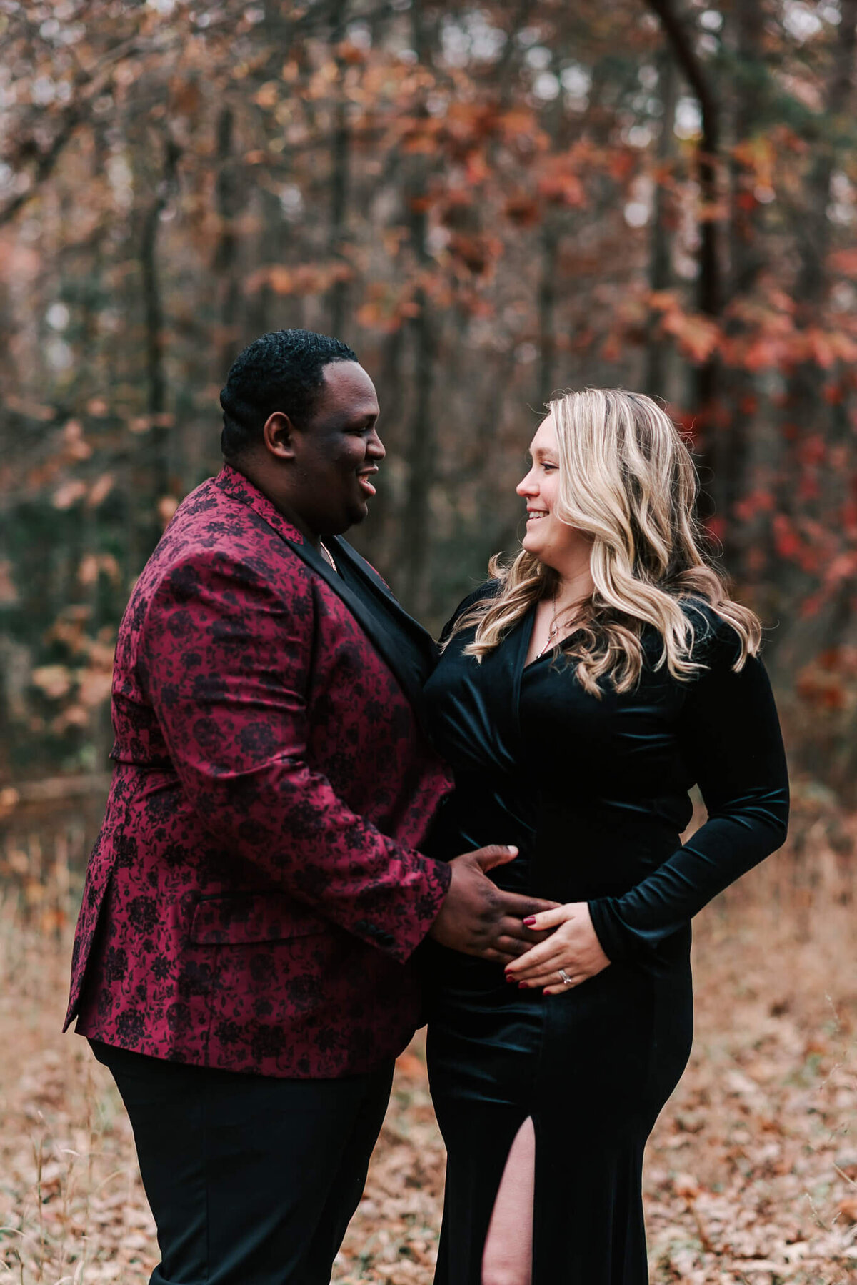 A pregnant woman clad in black and a man in burgundy smiling happily at each other