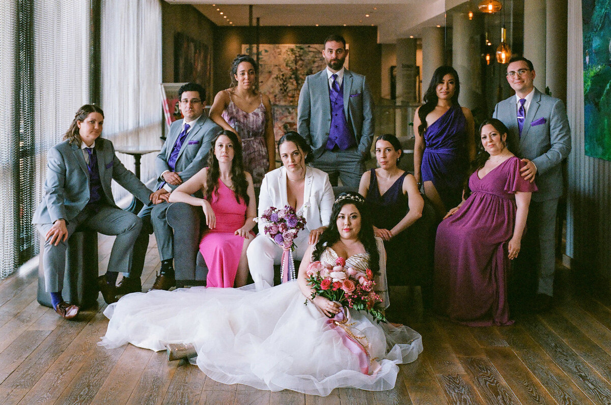 A bride sitting on the floor with the wedding party around them.
