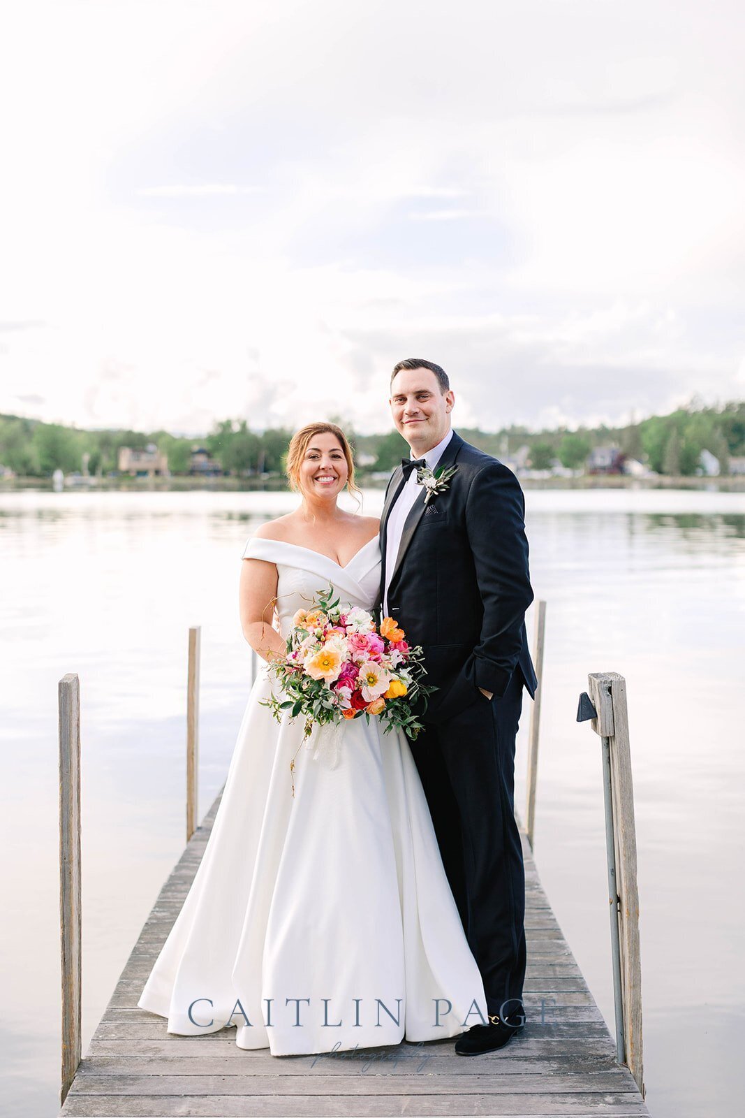 Couple with bridal bouquet standing on the dock at Mill Falls