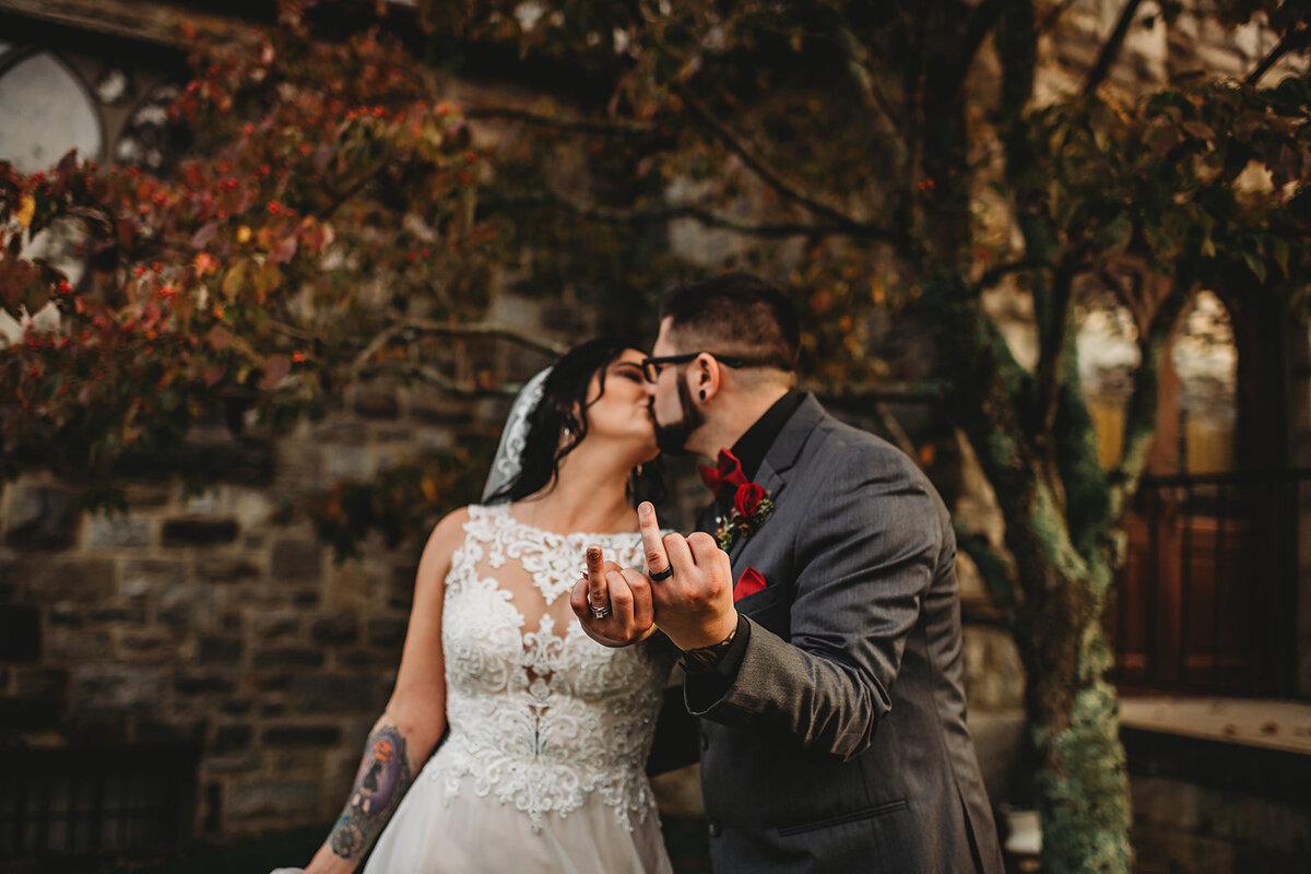 Maryland wedding photographer captures fun wedding photos of bride and groom kissing each other while holding up the ring fingers to the camera to show off their wedding bands for their Baltimore wedding