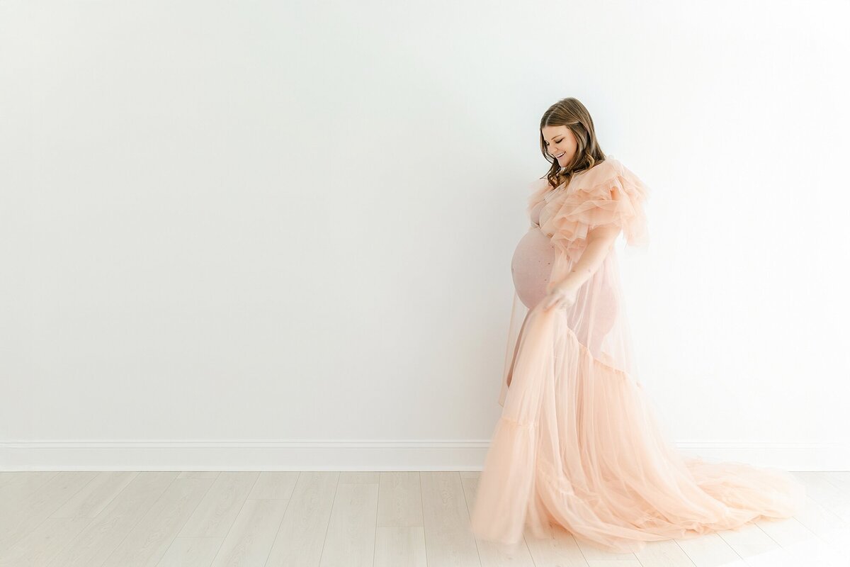 pregnant mom in pink tulle dress walking across studio