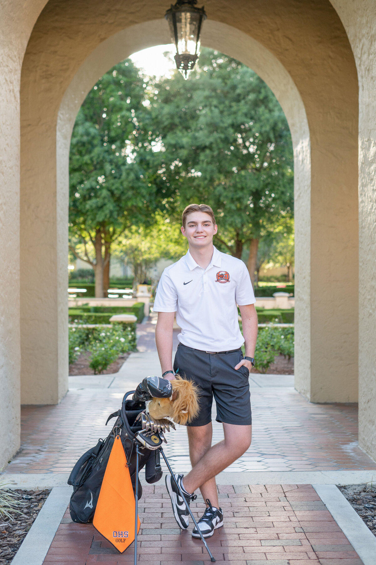 High school senior boy posing with golf clubs in archway.